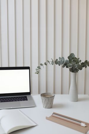 Computer on table beside flower vase and open notebooks