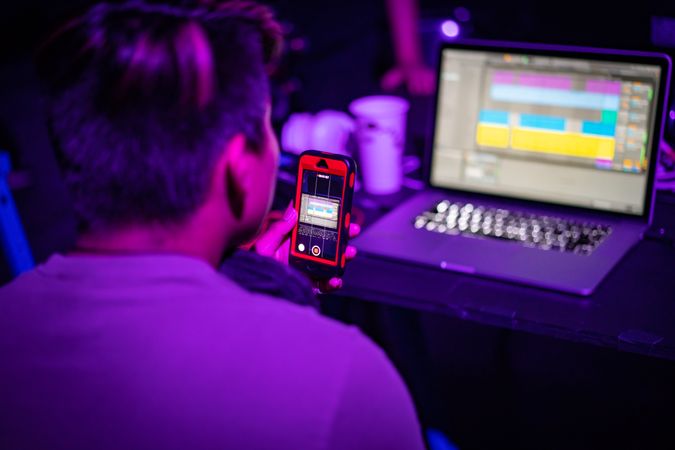 Man holding a phone and looking at a laptop in UV lit room