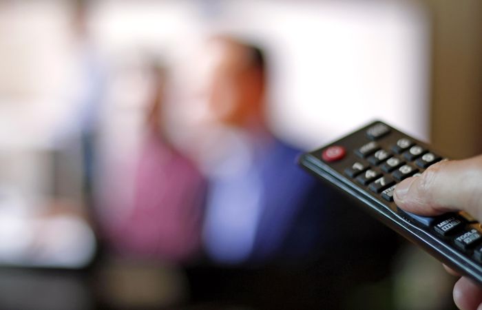 Person holding remote control with blurry image on TV screen